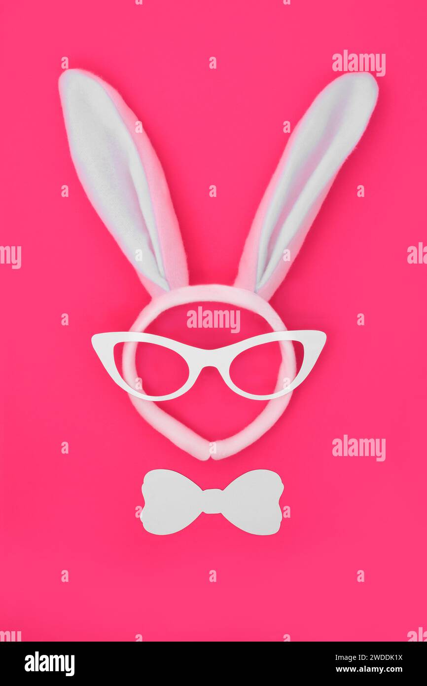 Fascia per orecchie coniglietto pasquale con occhiali e cravatta su sfondo rosa brillante. Design astratto surreale, divertente e minimalista per le festività natalizie. Foto Stock
