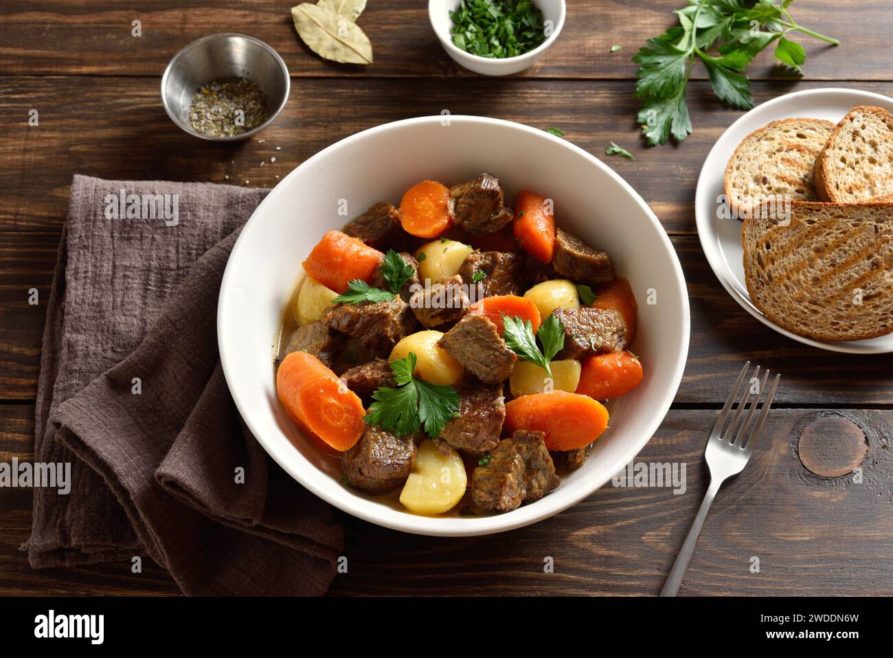 Carne di manzo stufata con patate, carote e spezie in un recipiente bianco su fondo di legno. Cibo salutare di conforto per cena. Vista ravvicinata Foto Stock