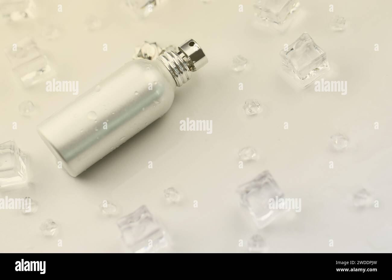 Bottiglia argentata di profumo femminile, fotografia oggettiva della bottiglia di profumo metallico in cubetti di ghiaccio e acqua su tavolo bianco. Vista dall'alto. Foto del prodotto mockup, concetto di freschezza e aroma Foto Stock