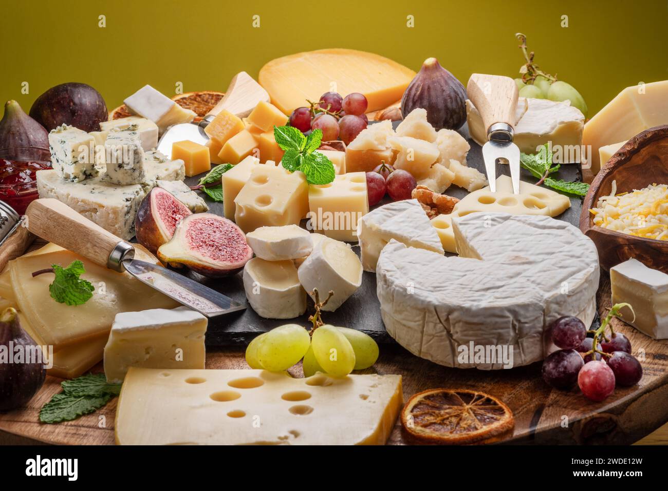 Varietà di formaggi a fette con frutta, menta, noci e taglierini. Un meraviglioso sfondo di formaggi per i vostri progetti. Foto Stock