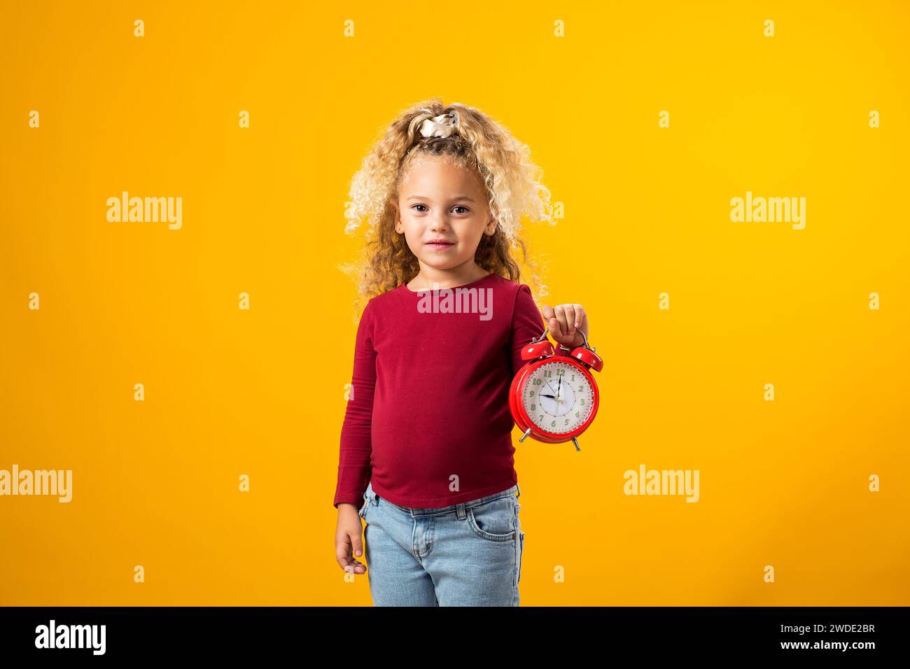 Giovane ragazza che tiene una sveglia, simboleggia la gestione del tempo, l'istruzione, la scuola e l'urgenza di scadenze e studi." Foto Stock