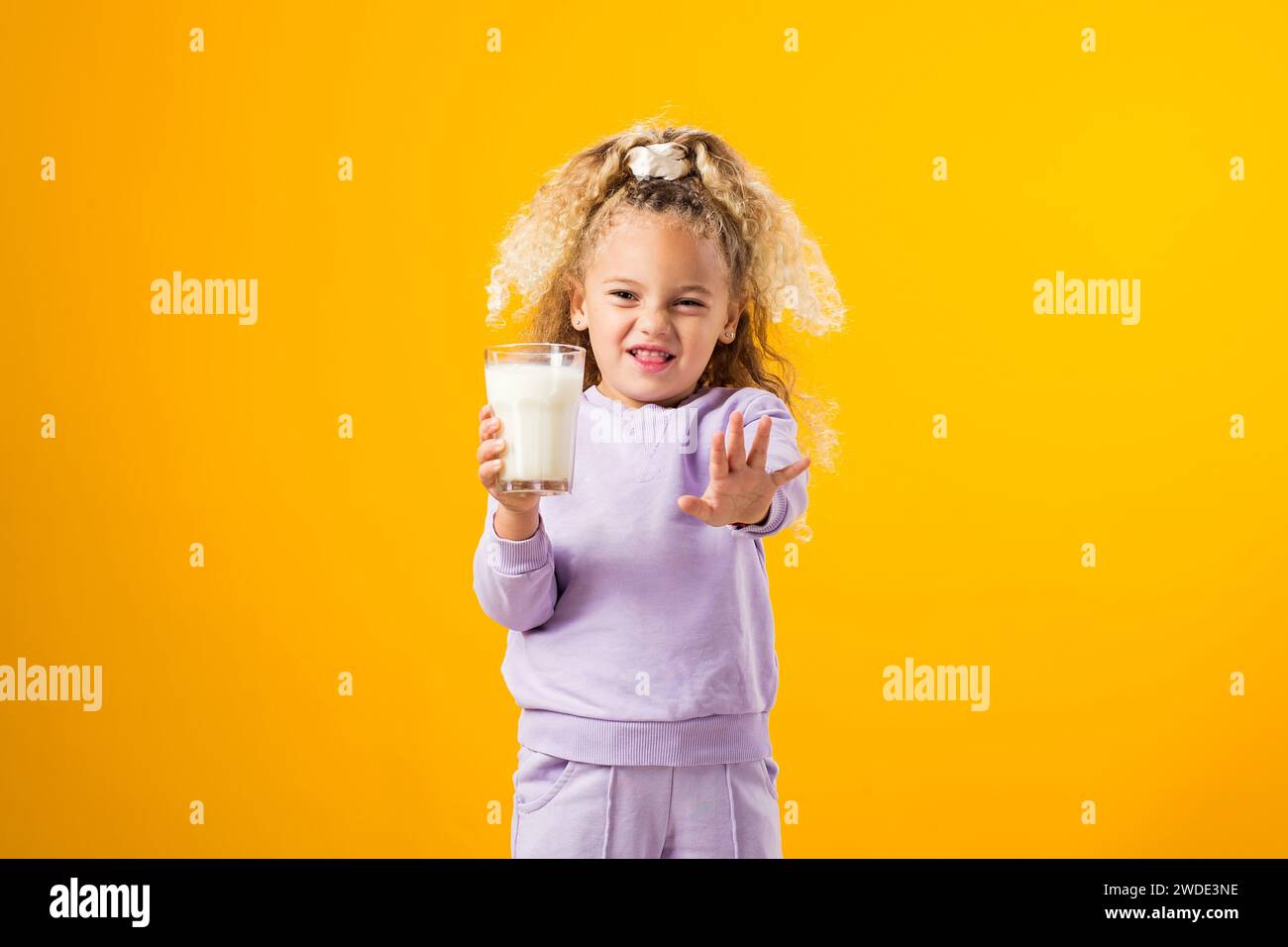 Fastidio da latte: Ragazza espressiva che regge un bicchiere di latte, che illustra l'intolleranza al lattosio e l'importanza dell'assistenza sanitaria. Espressione sgradevole r Foto Stock