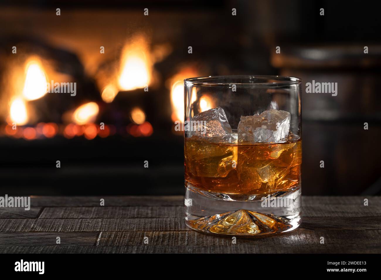 Bicchiere di whisky e ghiaccio su un tavolo di legno con caminetto in fiamme sullo sfondo Foto Stock