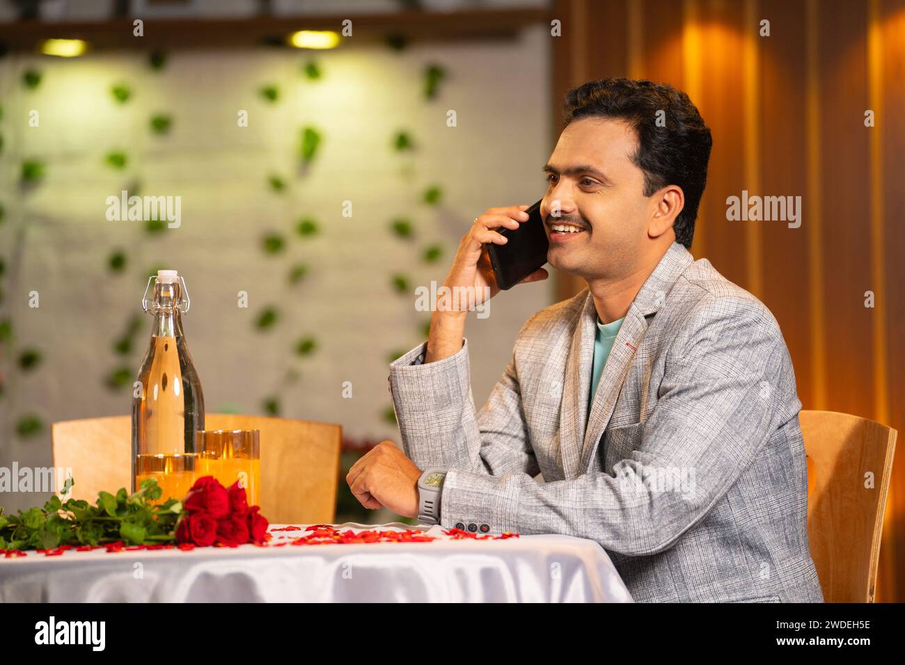 Un uomo indiano di mezza età che parla al telefono con la moglie per una cena a lume di candela a sorpresa al ristorante - concetto di pianificazione dell'anniversario e sorpresa Foto Stock