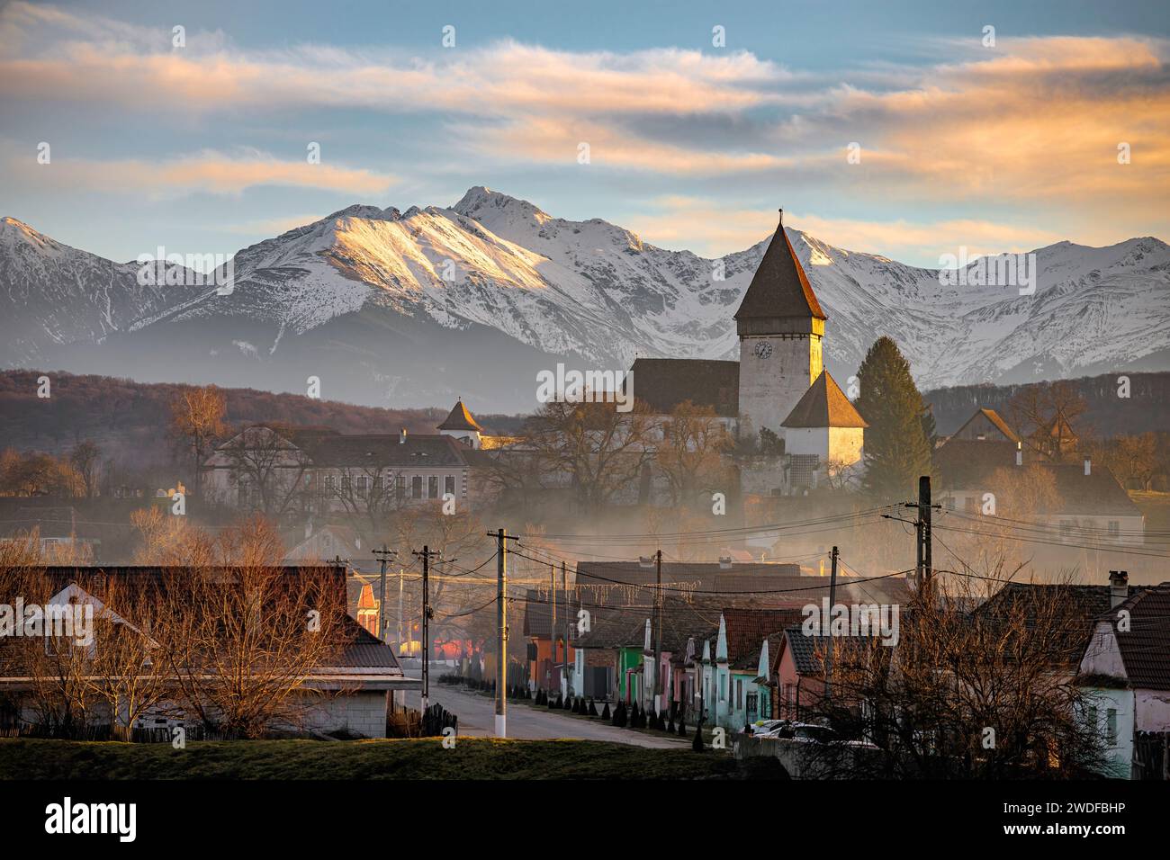 La chiesa fortificata di Hosman e il villaggio all'ora d'oro del tramonto. Foto scattata il 28 dicembre 2023 a Hosman, regione della Transilvania, Romania. Foto Stock