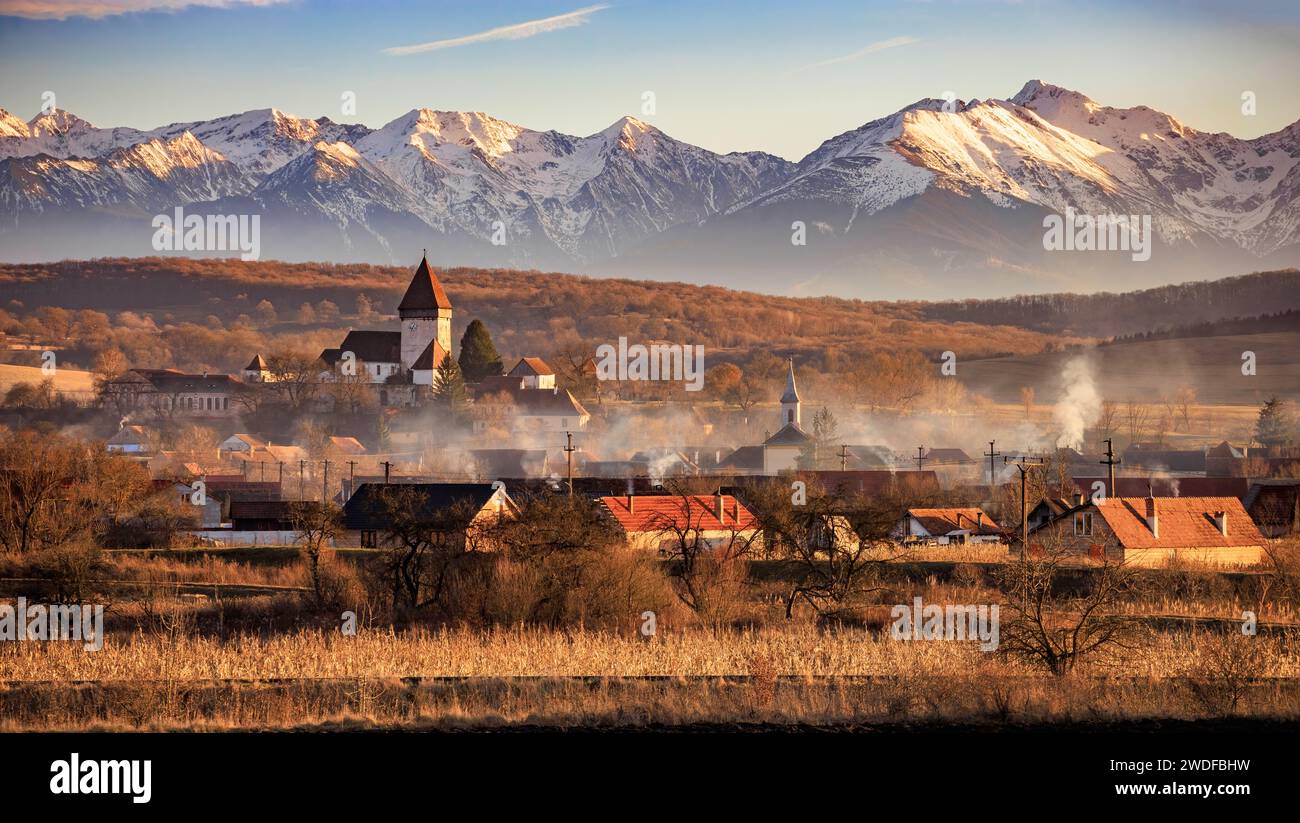 La chiesa fortificata di Hosman e il villaggio all'ora d'oro del tramonto. Foto scattata il 28 dicembre 2023 a Hosman, regione della Transilvania, Romania. Foto Stock