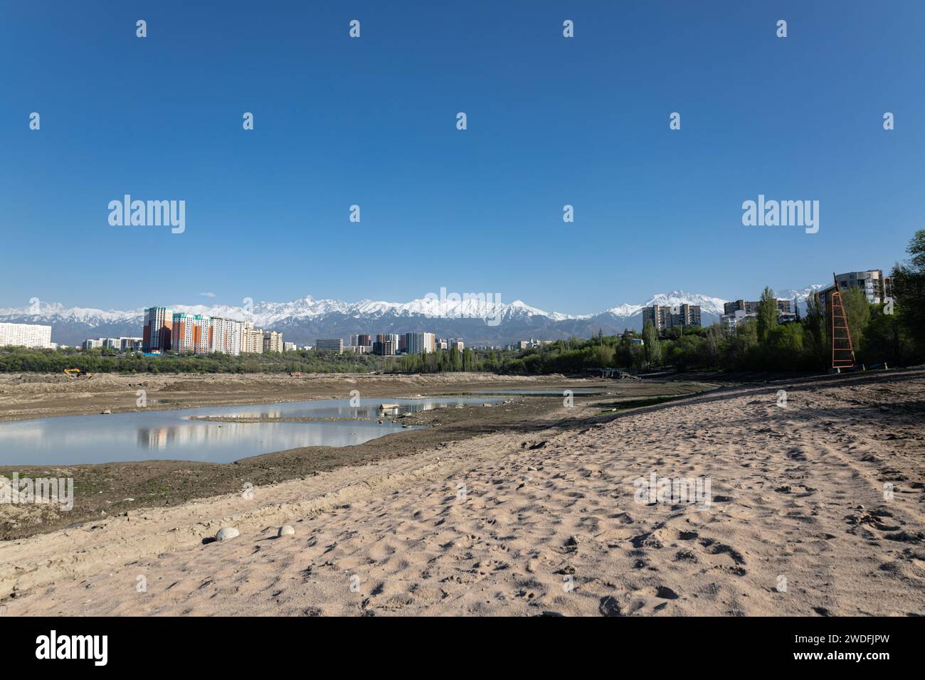 Serbatoio di stoccaggio Lago Sayran, Almaty, Kazakistan. Spiaggia di sabbia di Empty City con laghetto drenato. Edifici residenziali e alta cima innevata Foto Stock