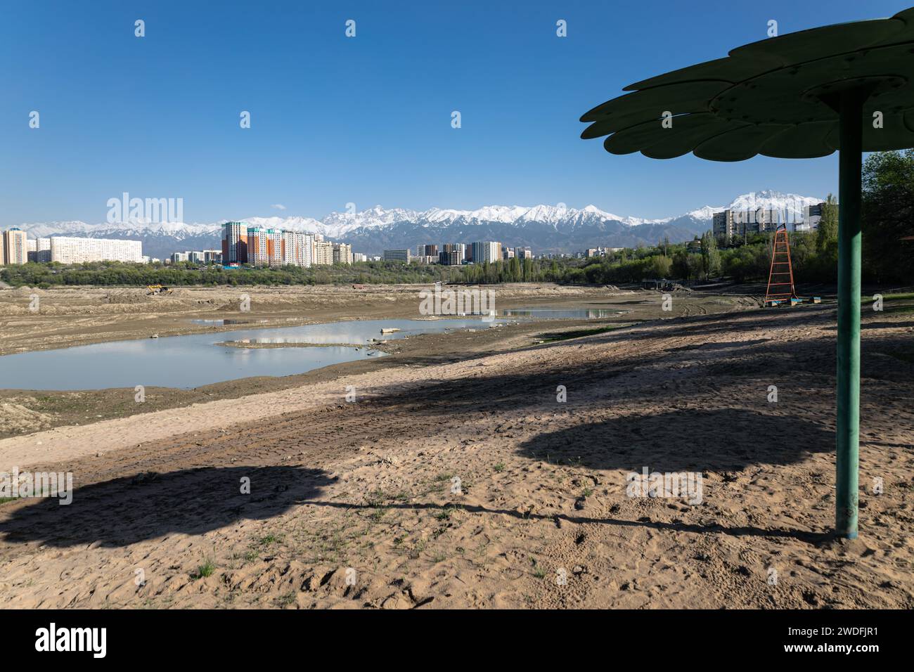 Spiaggia di sabbia di Empty City con laghetto drenato. Ombrelloni fissi in metallo. Edifici residenziali e alte montagne innevate sullo sfondo. Foto Stock