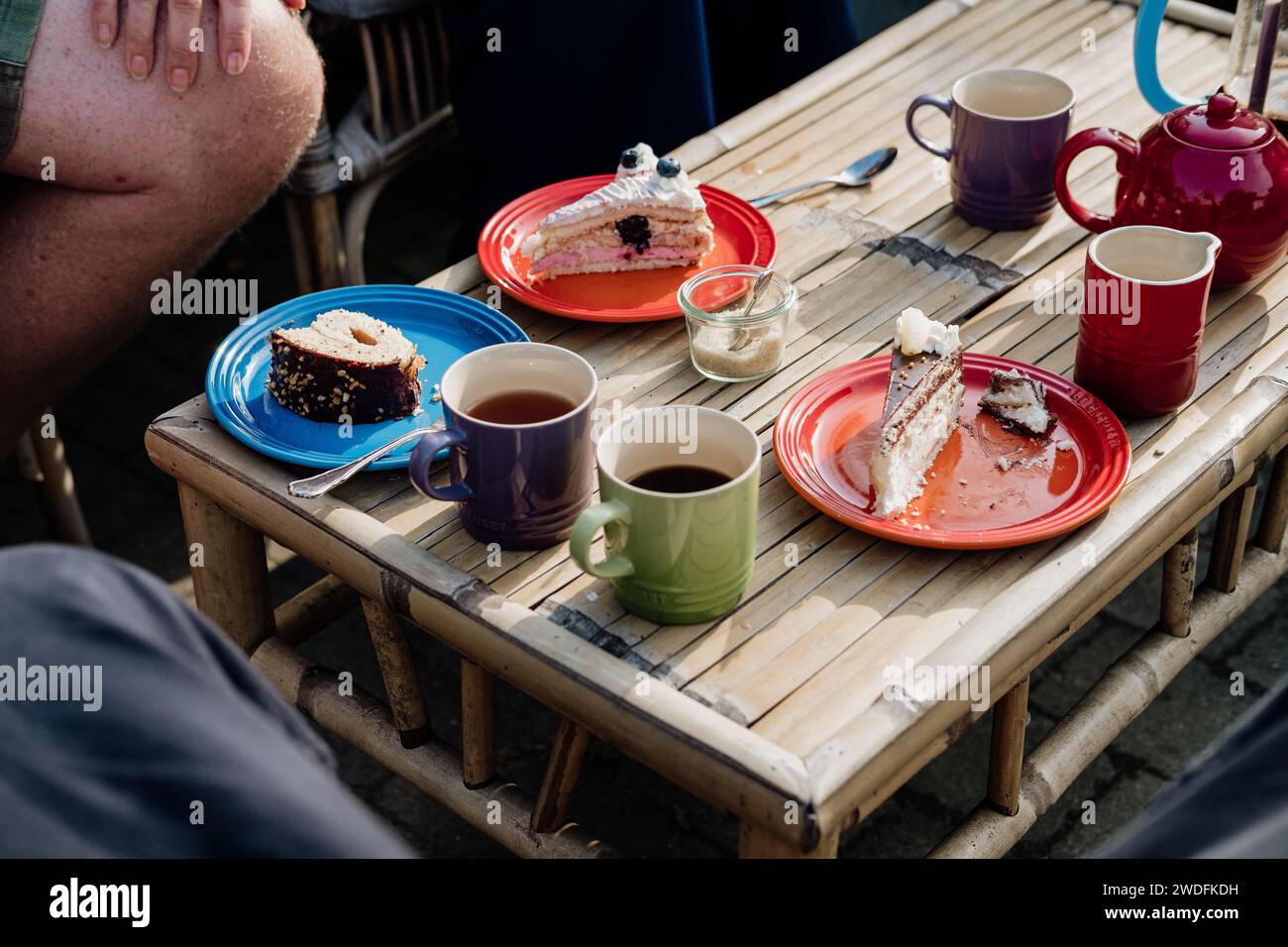 Tazze, piatti, fette di torta, teiera su un tavolo. Amici e parenti si uniscono per la torta di compleanno. Bere caffè e tè all'aperto in giardino. Foto Stock