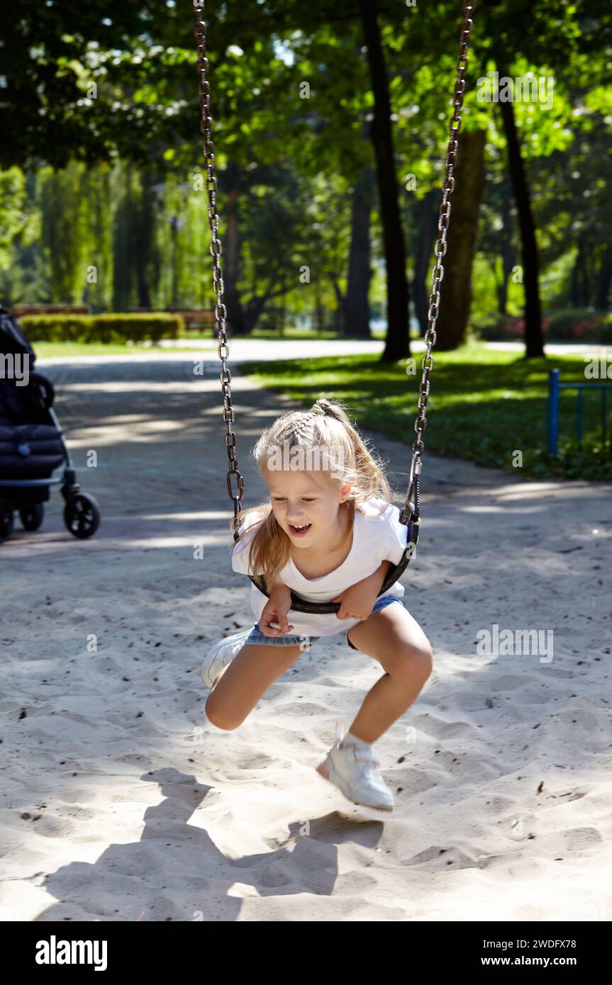 Una bambina che si alza su un parco giochi nel parco cittadino estivo. Concetto di infanzia, tempo libero e persone - buon riposo per i bambini e buon divertimento Foto Stock