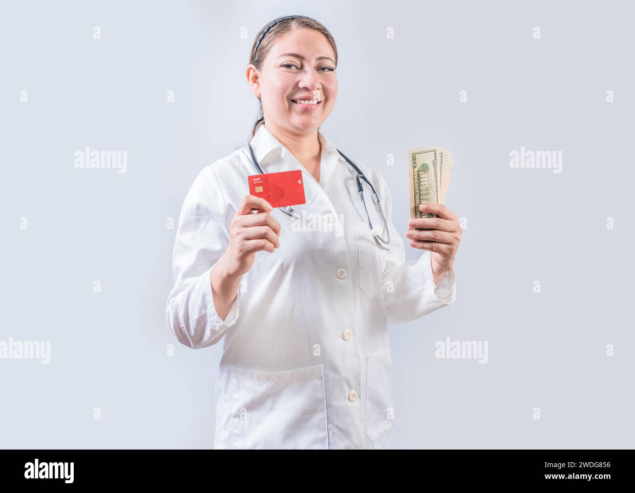 Bella e sorridente medico in possesso di denaro e carte di credito. Un medico felice che tiene in mano la carta di credito e denaro isolato Foto Stock