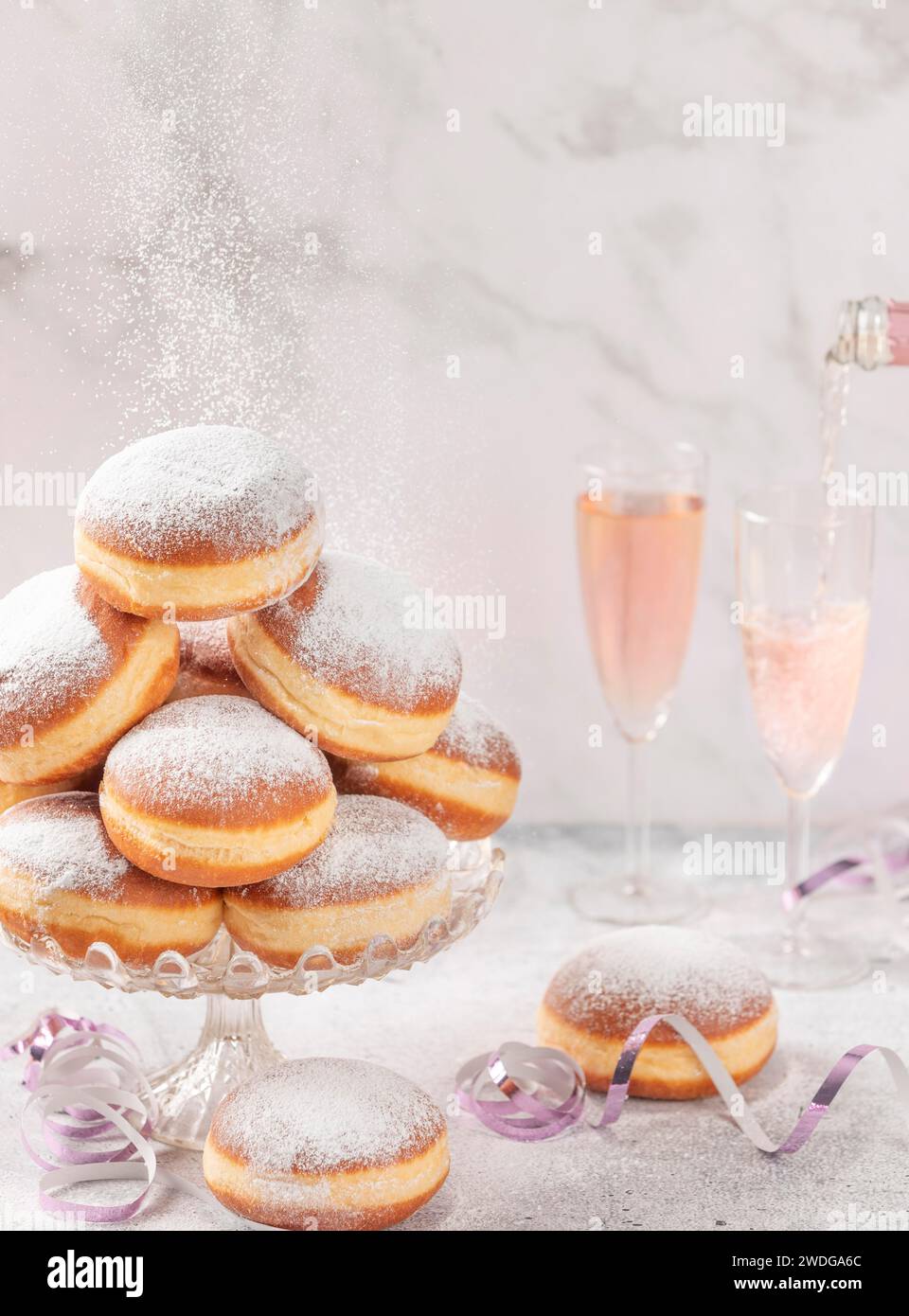 Gli impasti su un supporto di vetro, il vino frizzante rosa viene versato sullo sfondo, facendo cadere lo zucchero a velo Foto Stock