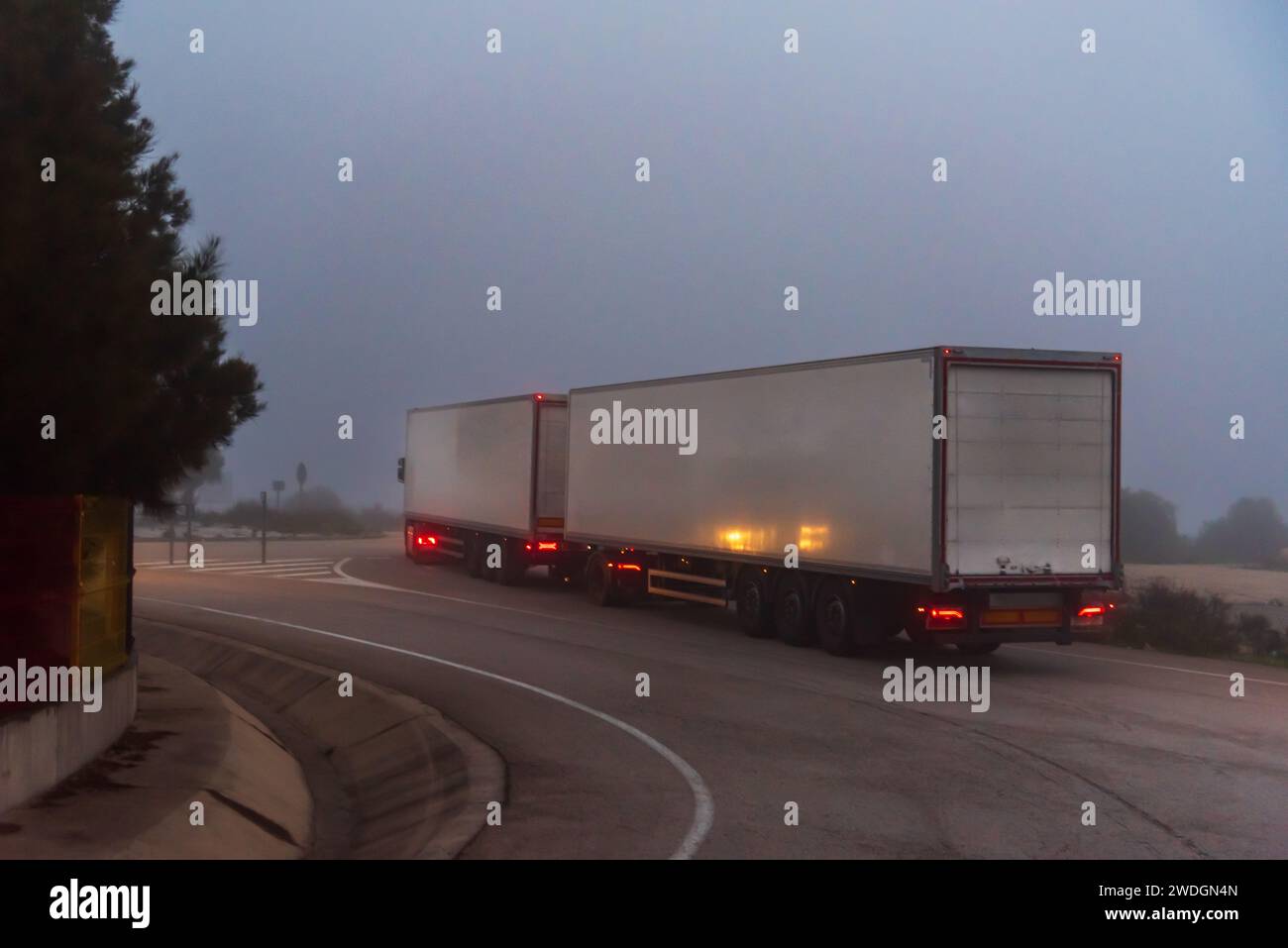 Un autocarro Duo-trailer che guida su una strada secondaria in una giornata nebbiosa. Foto Stock