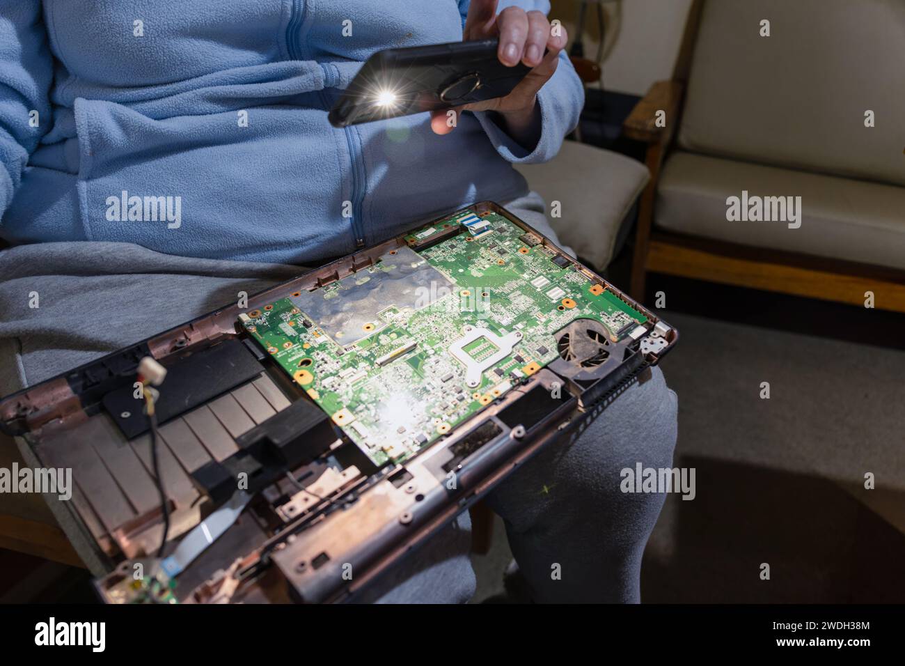 vecchia con un portatile in grembo e una torcia che cerca di ripararlo Foto Stock