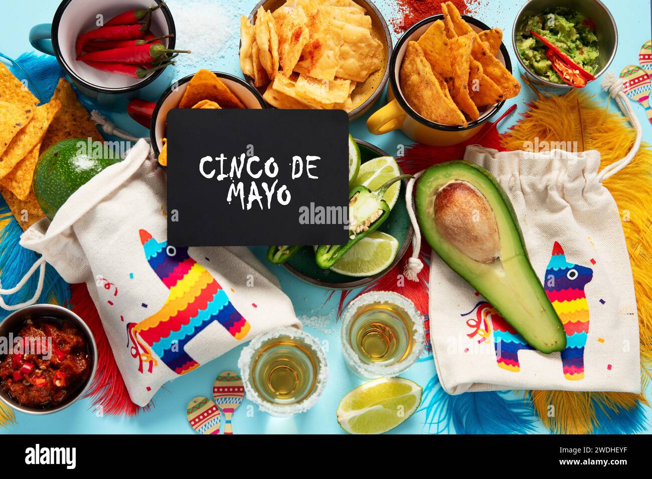 Concetto di Cinco-de-mayo. Piatto tradizionale nacho chips salsa peperoncino tequila con sale lime sombrero serape cactus e maracas su sfondo blu. Foto Stock