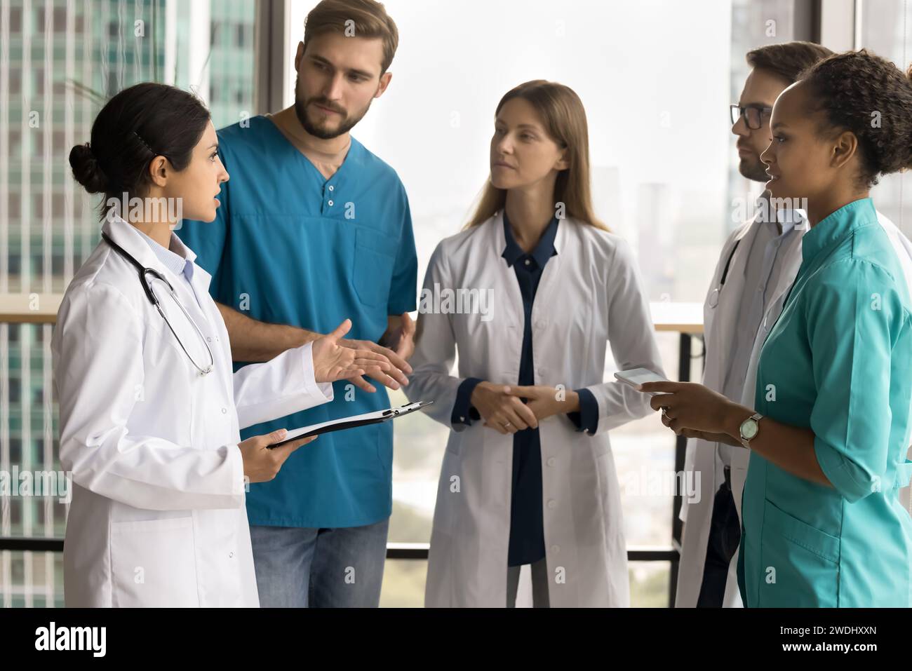 Serio giovane medico indiano che parla con personale medico diverso Foto Stock