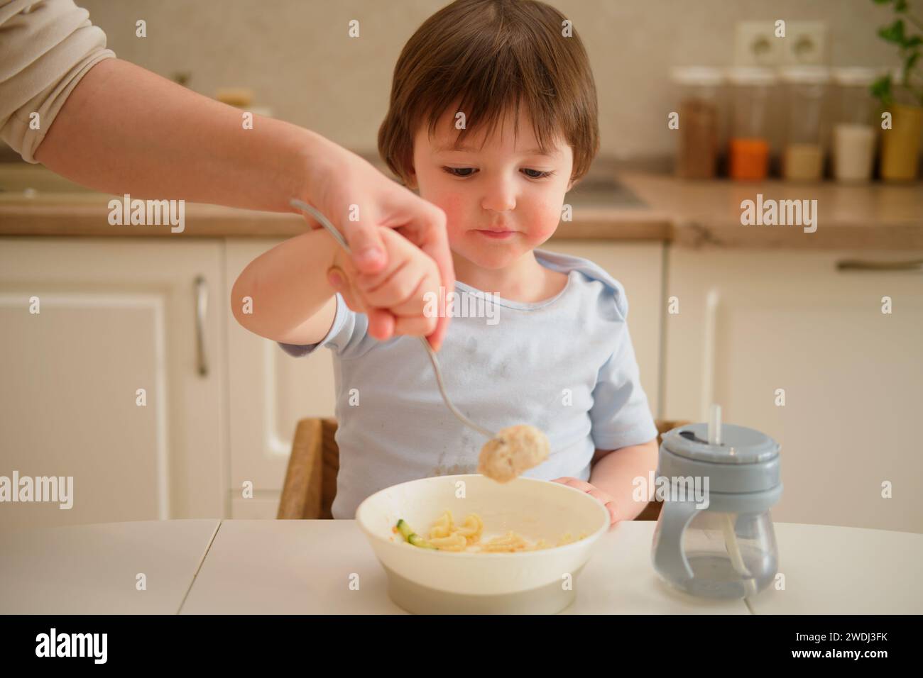 La madre insegna al bambino a mangiare con una forchetta in cucina. Mamma e figlio cucinano insieme in cucina. Bimbo di due anni a D. Foto Stock