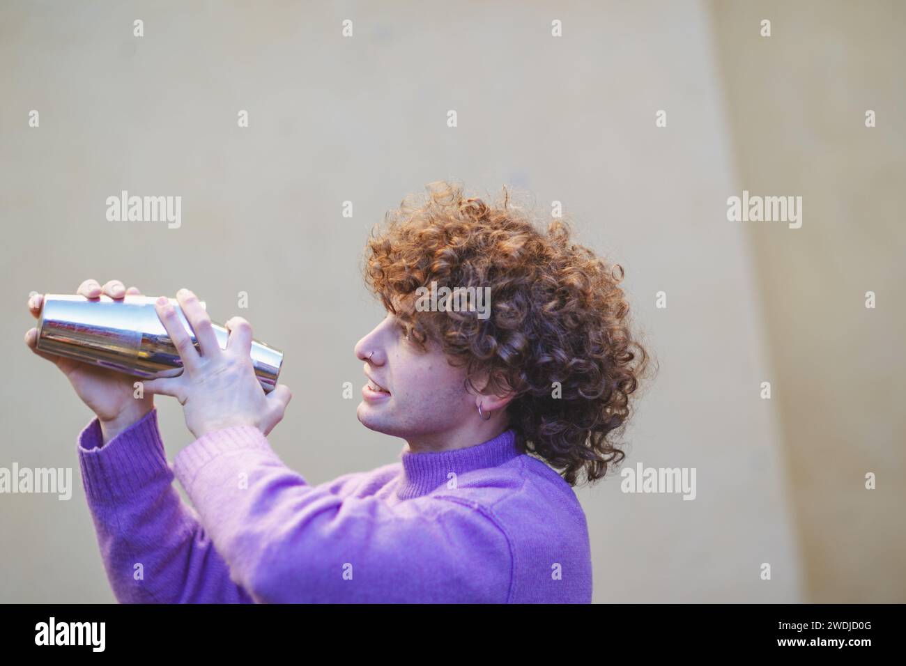 giovane barista caucasico dai capelli rossi freschi che mescola un cocktail in shaker con energia all'aperto in un evento privato in inverno Foto Stock