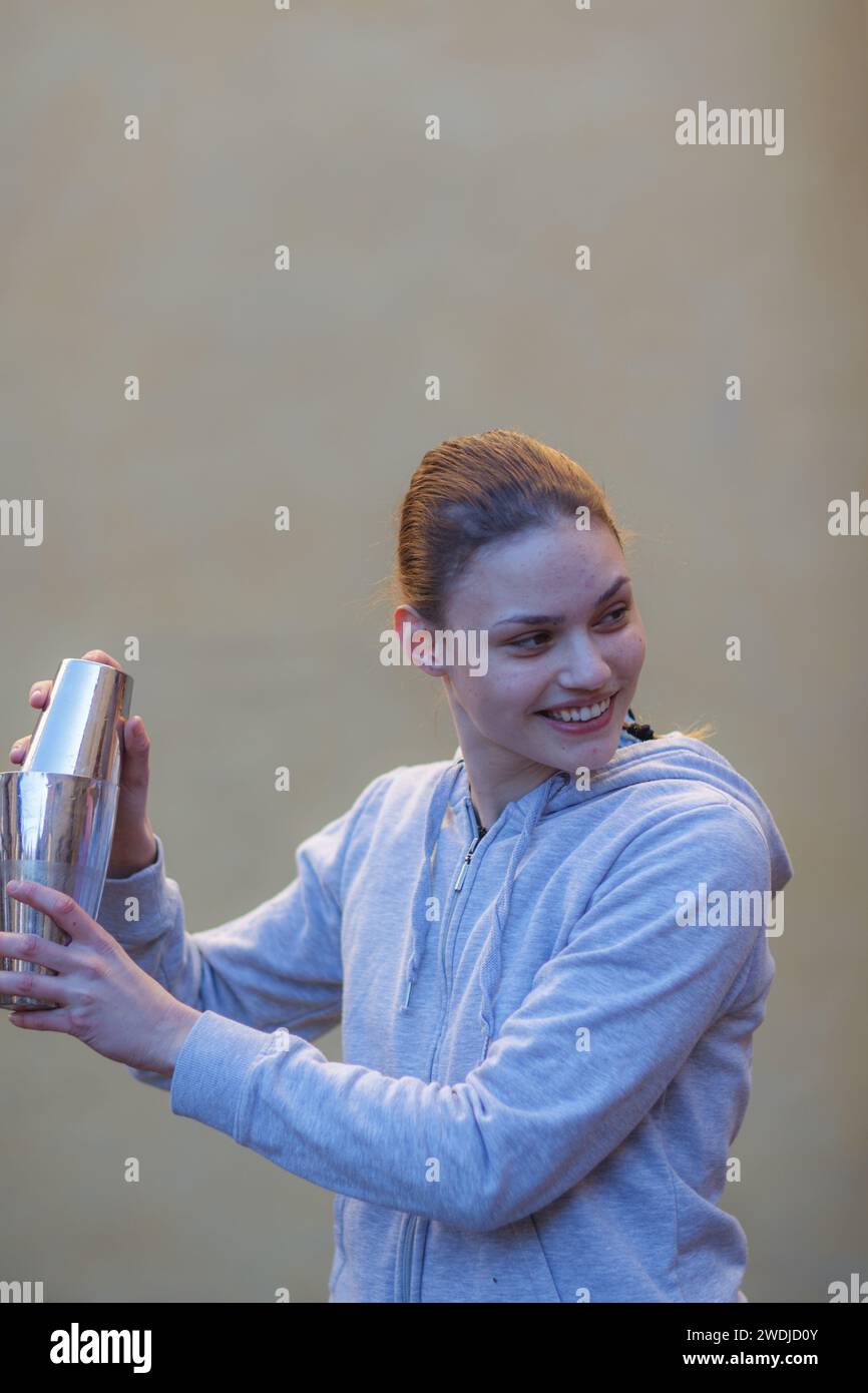giovane barista caucasico dai capelli rossi freschi che mescola un cocktail in shaker con energia all'aperto in un evento privato in inverno Foto Stock