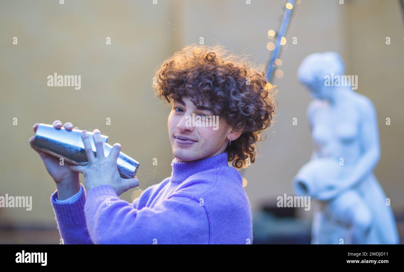 giovane barista caucasico dai capelli rossi freschi che mescola un cocktail in shaker con energia all'aperto in un evento privato in inverno Foto Stock