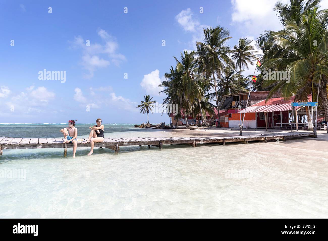 Madre e figlio, turisti, seduti su un molo di legno su una spiaggia sabbiosa, godendosi le vacanze su un'isola tropicale, sull'arcipelago di San Blas, Panama Foto Stock