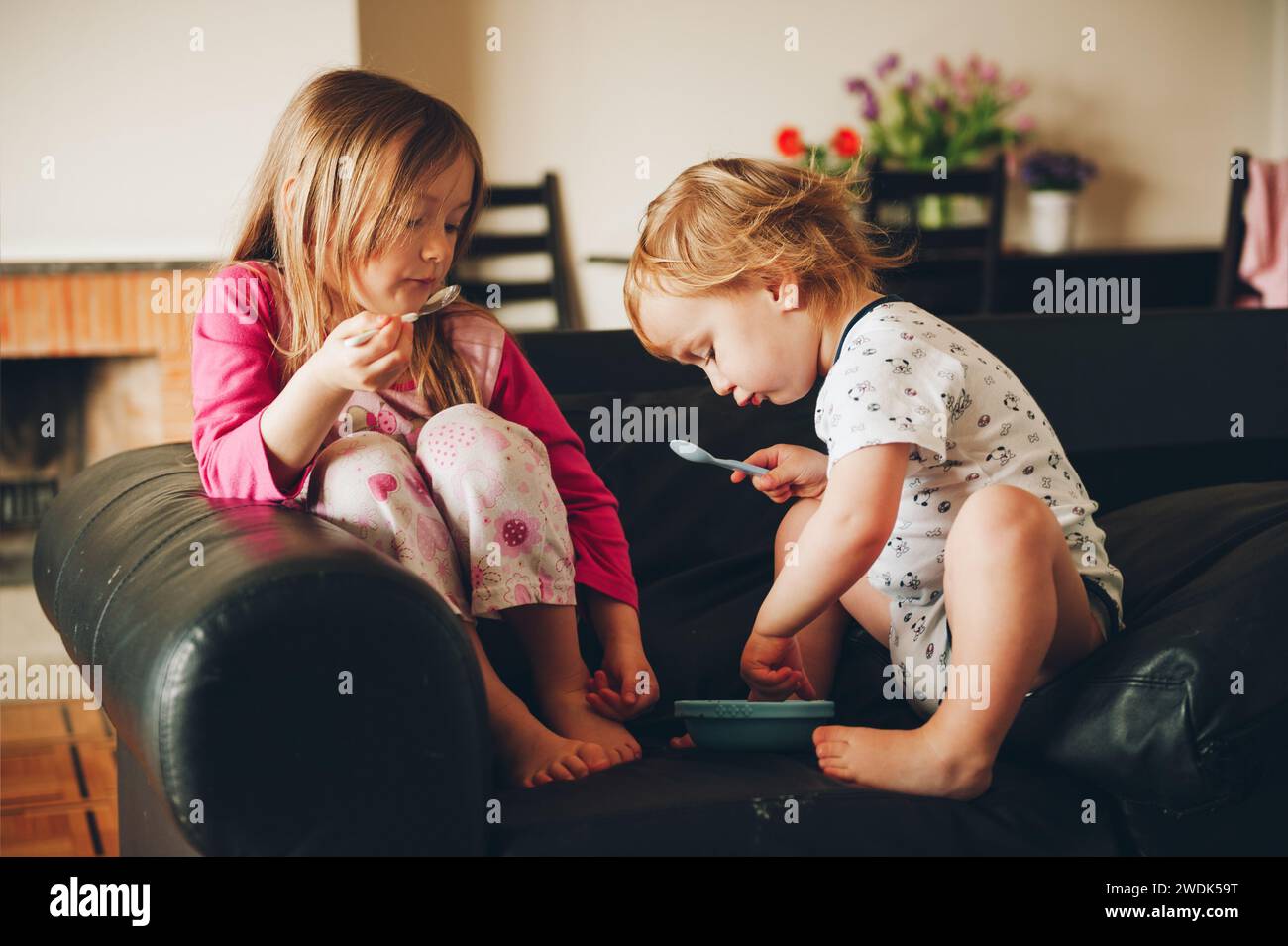 Due bambini disordinati che mangiano da un piatto appoggiati sul divano Foto Stock