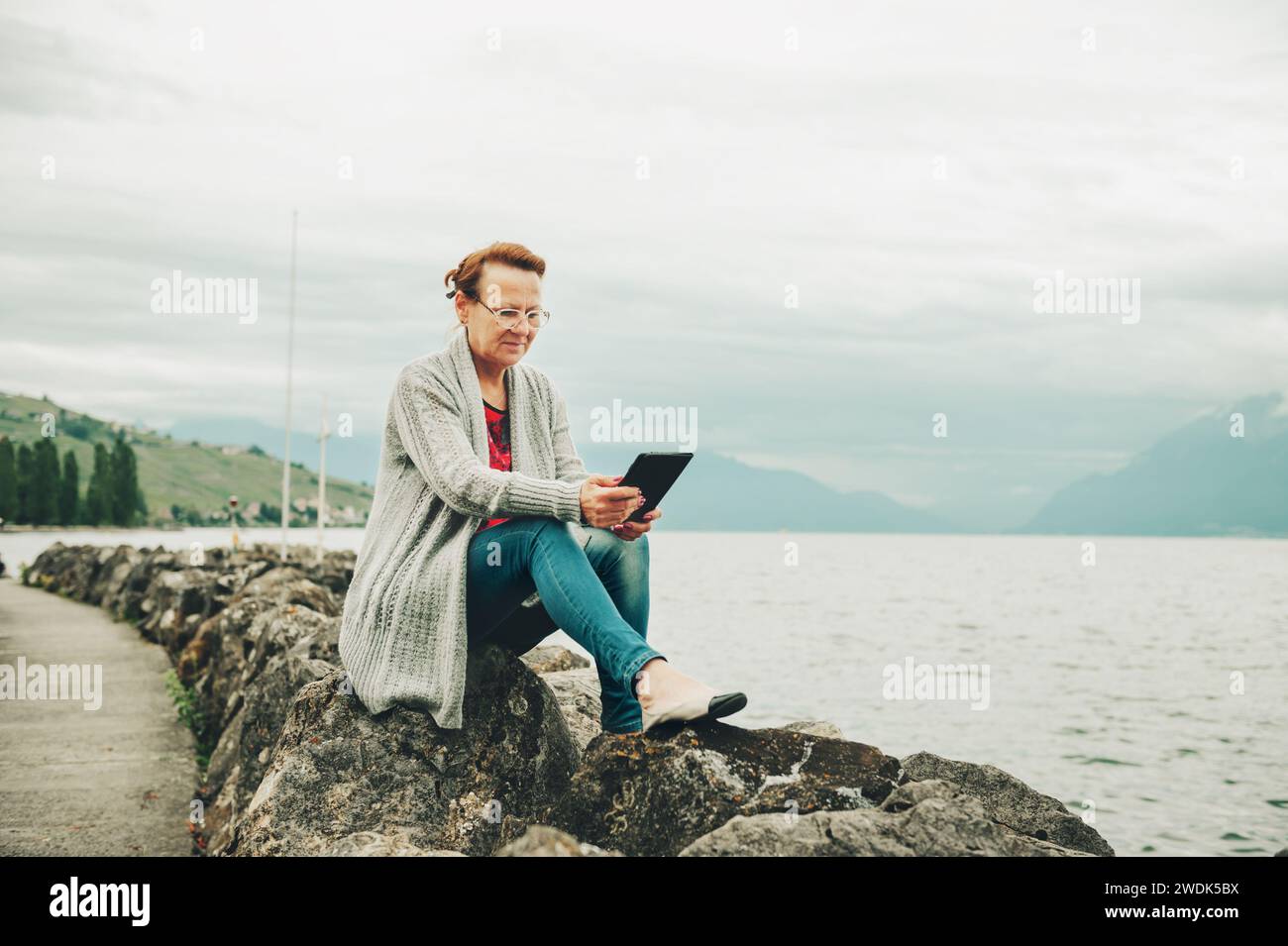 Donna di mezza età che riposa vicino al lago, che usa un tablet pc all'aperto Foto Stock