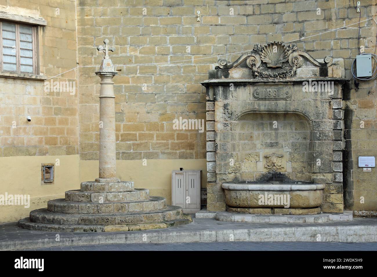 Fontana d'acqua datata 1881 e croce in pietra a Victoria a Gozo Foto Stock