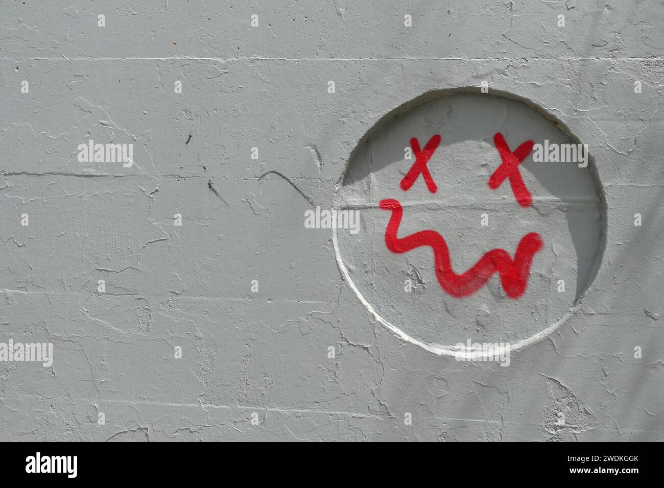 Semplice faccia sorridente con bocca storta verniciata a spruzzo su incavo a parete grigio. Sfondo astratto. Foto Stock