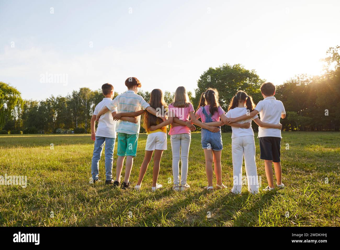 Un gruppo di bambini adolescenti guarda il tramonto insieme durante la passeggiata estiva nel parco verde. Foto Stock