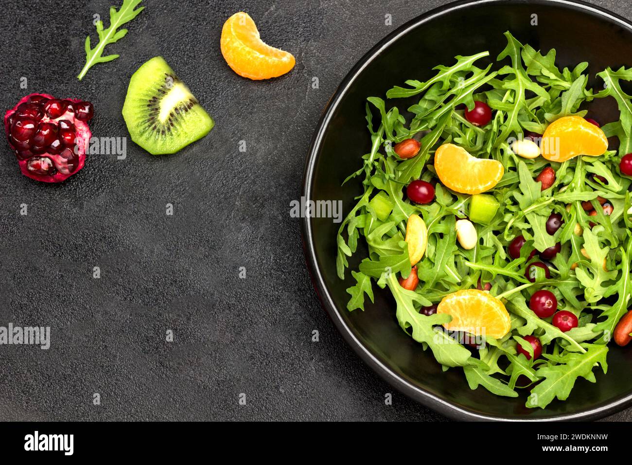 Macedonia di frutta con rucola, mandarini e semi di melograno. Dieta sana cibo vegetariano. Spianatura piatta. Sfondo nero. Foto Stock