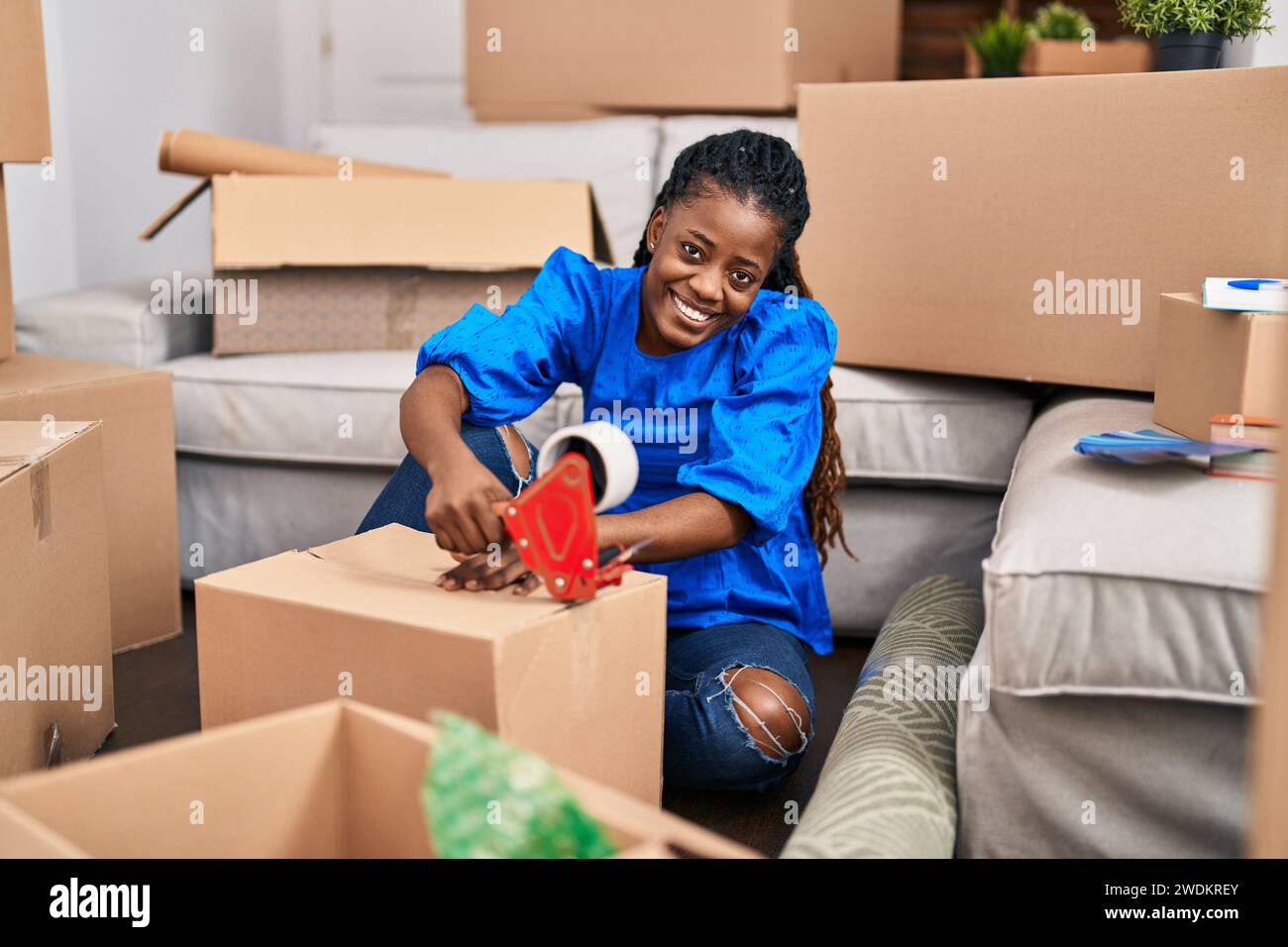 Donna afroamericana sorridente sicuro imballaggio scatola di cartone in nuova casa Foto Stock