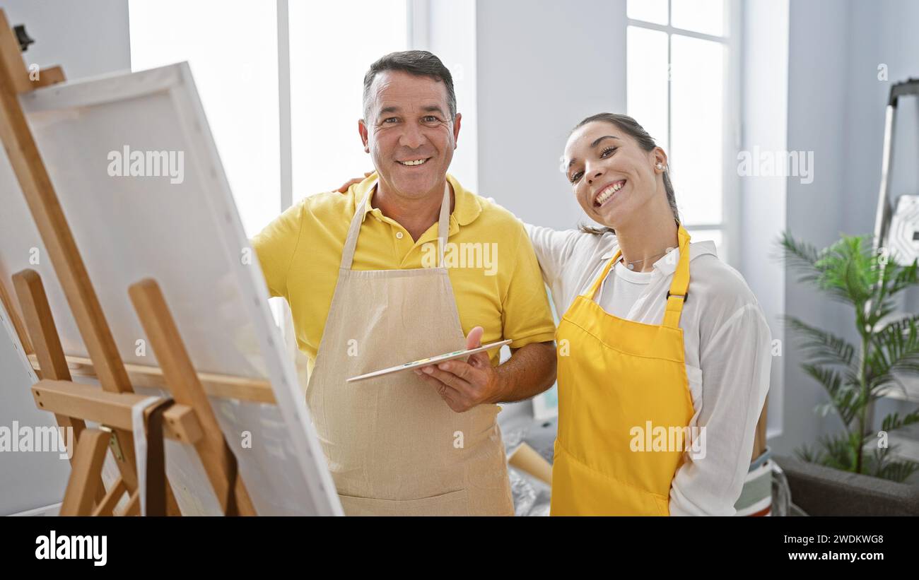 Sorridenti artisti maschili e femminili che si abbracciano gioiosamente in uno studio d'arte, disegnano insieme e abbracciano la creatività Foto Stock