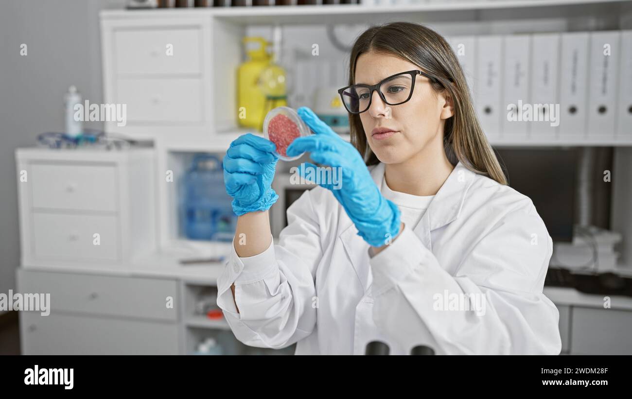 Una giovane scienziata esamina un piatto di Petri con un campione in un moderno laboratorio. Foto Stock