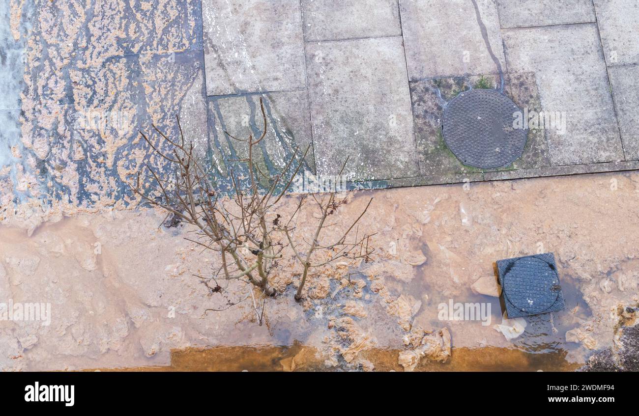 Primo piano a un problema di drenaggio in cui i tubi sono ostruiti e le acque reflue marroni fuoriescono sulla strada Foto Stock