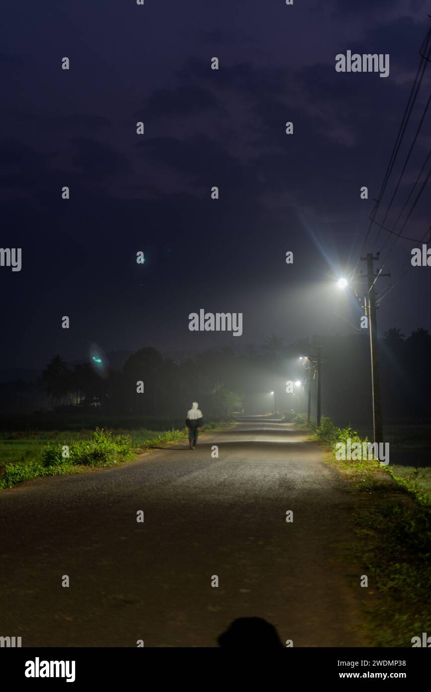 Una figura solitaria che passeggia lungo una strada inquietante sotto linee elettriche inquietanti Foto Stock