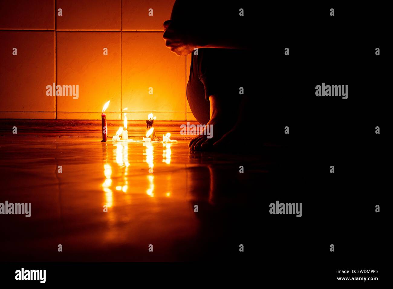 Una ragazza siede sul pavimento al buio con le candele in un appartamento al buio senza luce in Ucraina, seduta sul pavimento da sola al buio, piedi o Foto Stock