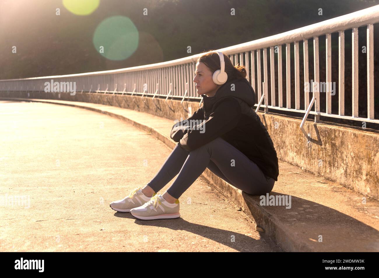 vesti donna sportiva seduta riposa dopo l'esercizio fisico e la corsa, indossando le cuffie. Foto Stock