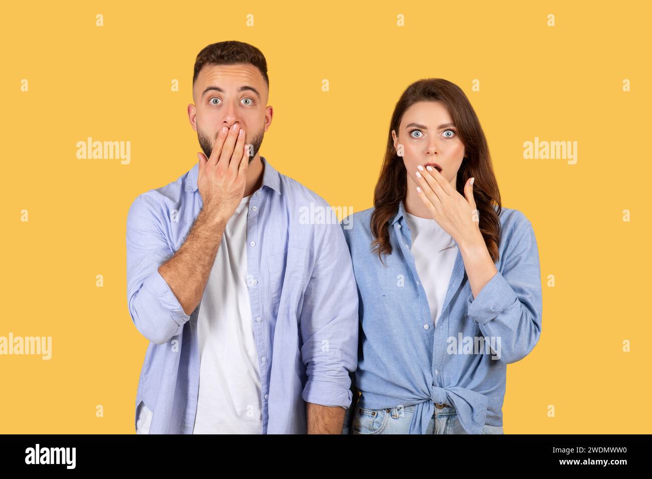 Coppia scioccata che copre le bocche, sorpresa con gli occhi larghi su sfondo giallo Foto Stock