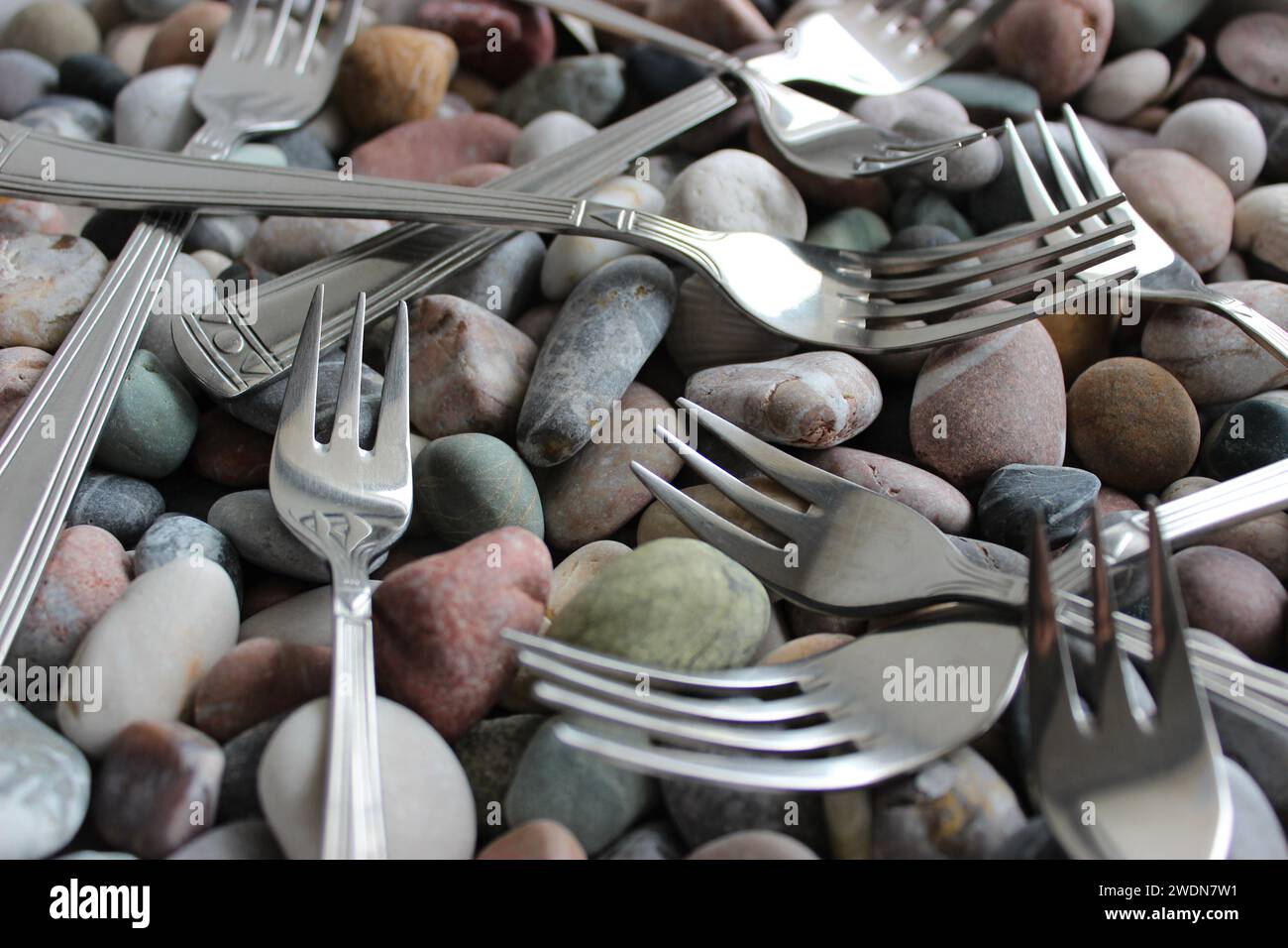 Forchette da tavolo e forchette per torta identiche del set di posate adagiate su piccole e lisce rocce marine Foto Stock