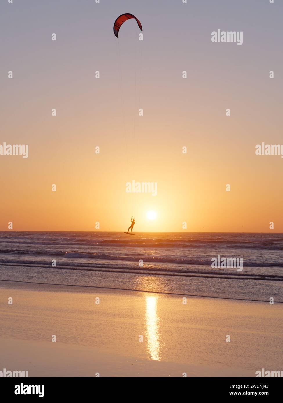 Kite surfer in aria al tramonto con un'isola alle spalle a Essaouira, Marocco, 21 gennaio 2024 Foto Stock