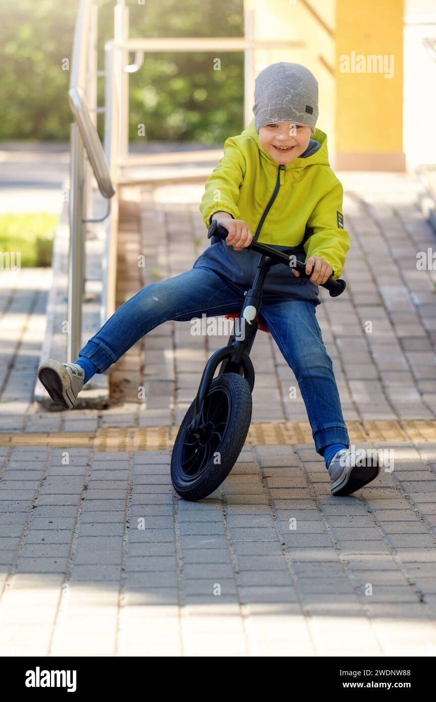 Bambini piccoli che si divertono in bici Balance in città, all'aperto. Scende lungo il pendio e impara ad equilibrarsi. Foto Stock