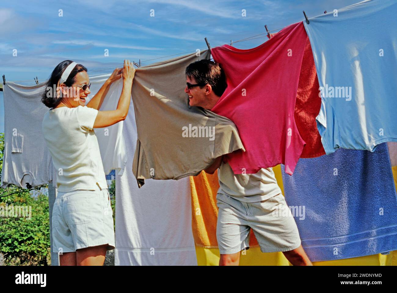 Una coppia che si prende gioco di un po' di vestiti puliti appesi all'aperto su una linea di abbigliamento Foto Stock