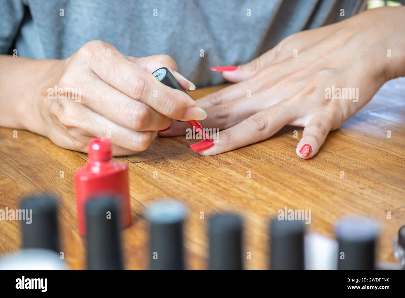 Mani di una giovane donna latina che dipinge le unghie con uno smalto rosso sul tavolo, circondata da accessori per la pittura. Foto Stock
