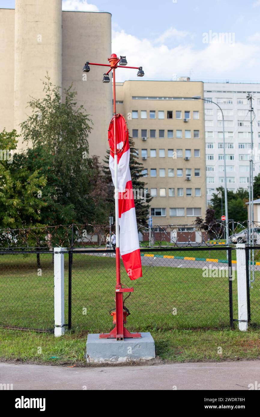 Mosca, regione di Mosca, Russia - 03.09.2023: Un indicatore di direzione del vento a strisce avvolto intorno al suo palo sul campo di aviazione con edifici sullo sfondo Foto Stock