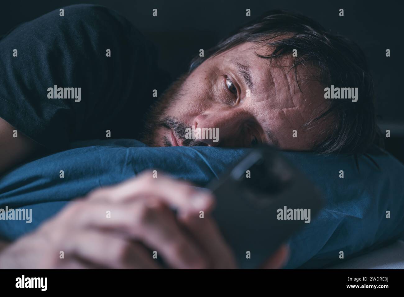 Uomo che usa lo smartphone mentre è sdraiato sul letto a tarda notte, concetto di insonnia, messa a fuoco selettiva Foto Stock