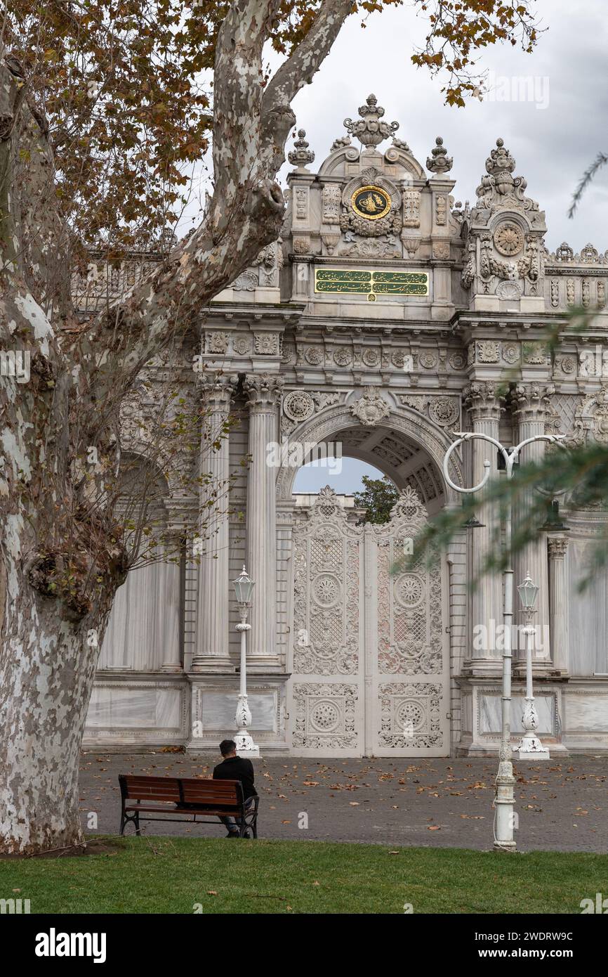 Uomo sulla panchina, di fronte al cancello bianco del Palazzo Dolmabahe Foto Stock
