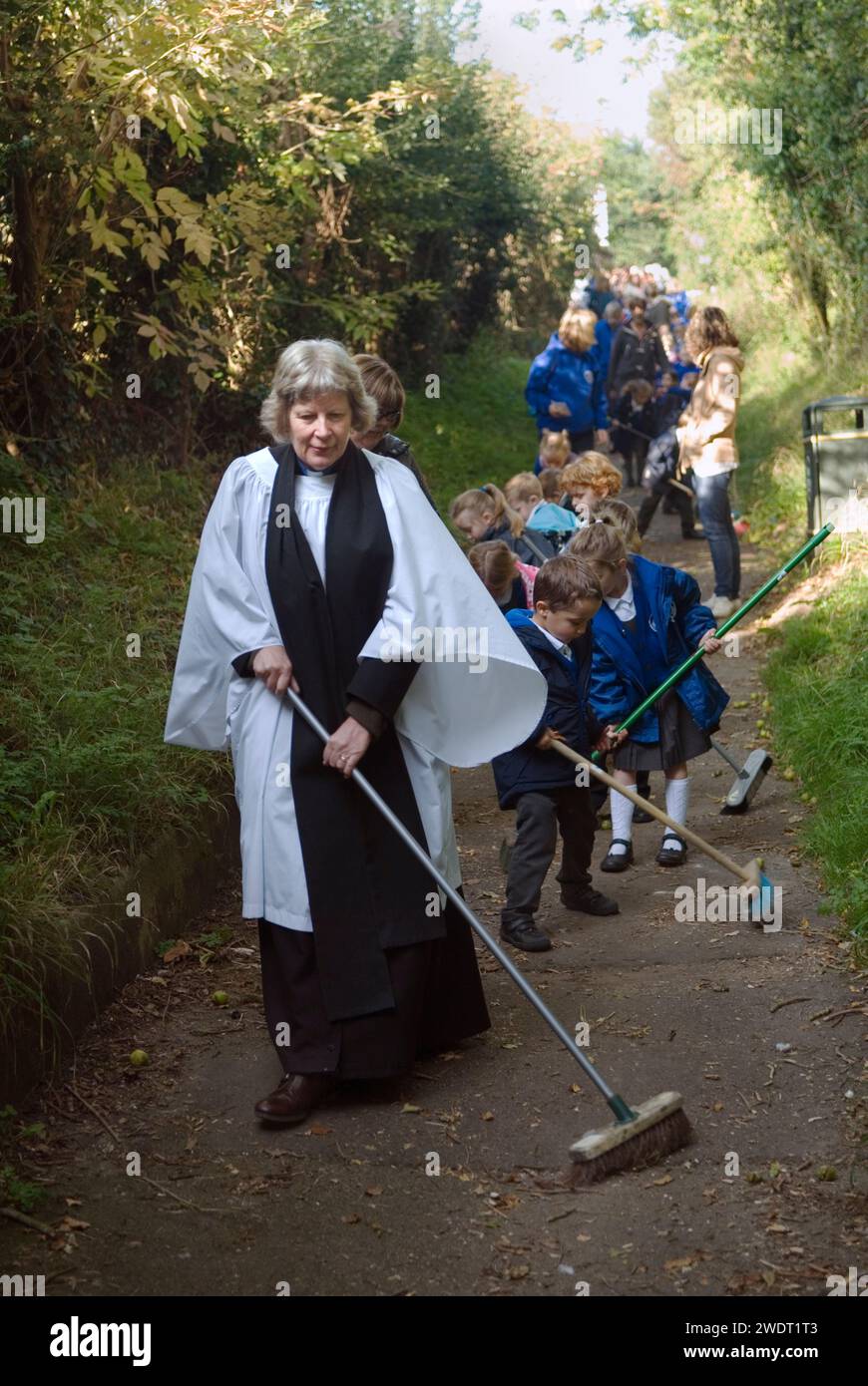 Old Mans Day Braughing, Hertfordshire, la Rev'd Julie Gawthrope spazza Fleece Lane dal Fleece Inn che conduce alla chiesa di St. Marys the Virgin con l'aiuto dei bambini della Jenyns First School. Inghilterra 1 ottobre 2015. HOMER SYKES, REGNO UNITO, ANNI '2010 Foto Stock