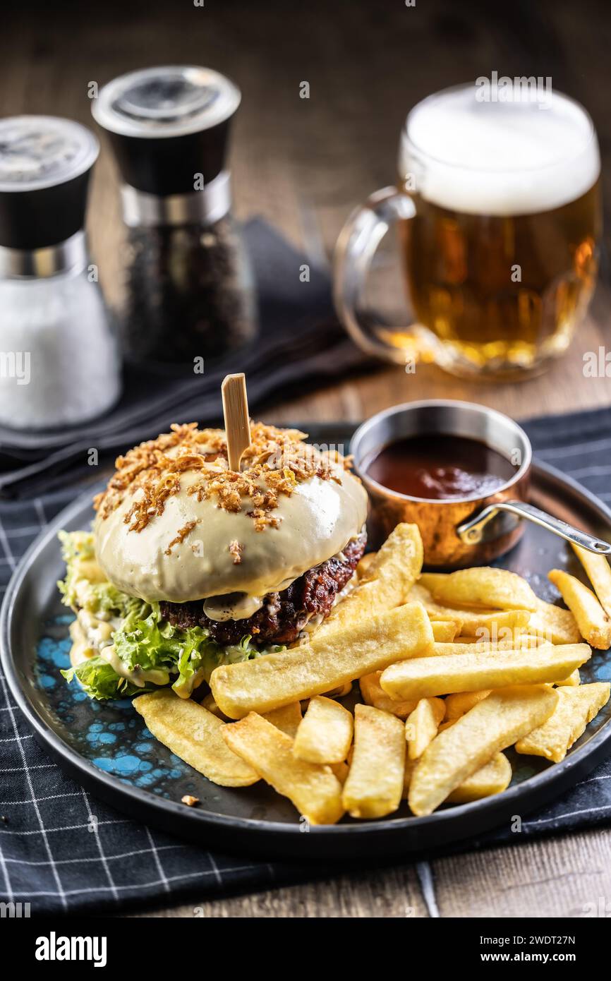 Hamburger di manzo con formaggio con patatine fritte e birra alla spina su un piatto da pub o ristorante. Foto Stock