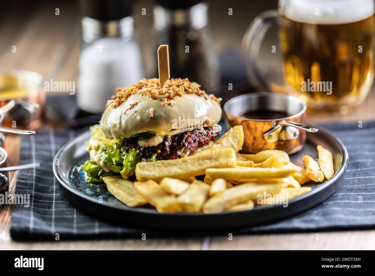Hamburger di manzo con formaggio con patatine fritte e birra alla spina su un piatto da pub o ristorante. Foto Stock
